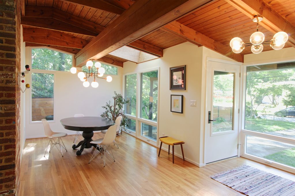 View of exposed structure and new floor to ceiling windows that make for a very inviting, very open mid-century modern entry and dining room